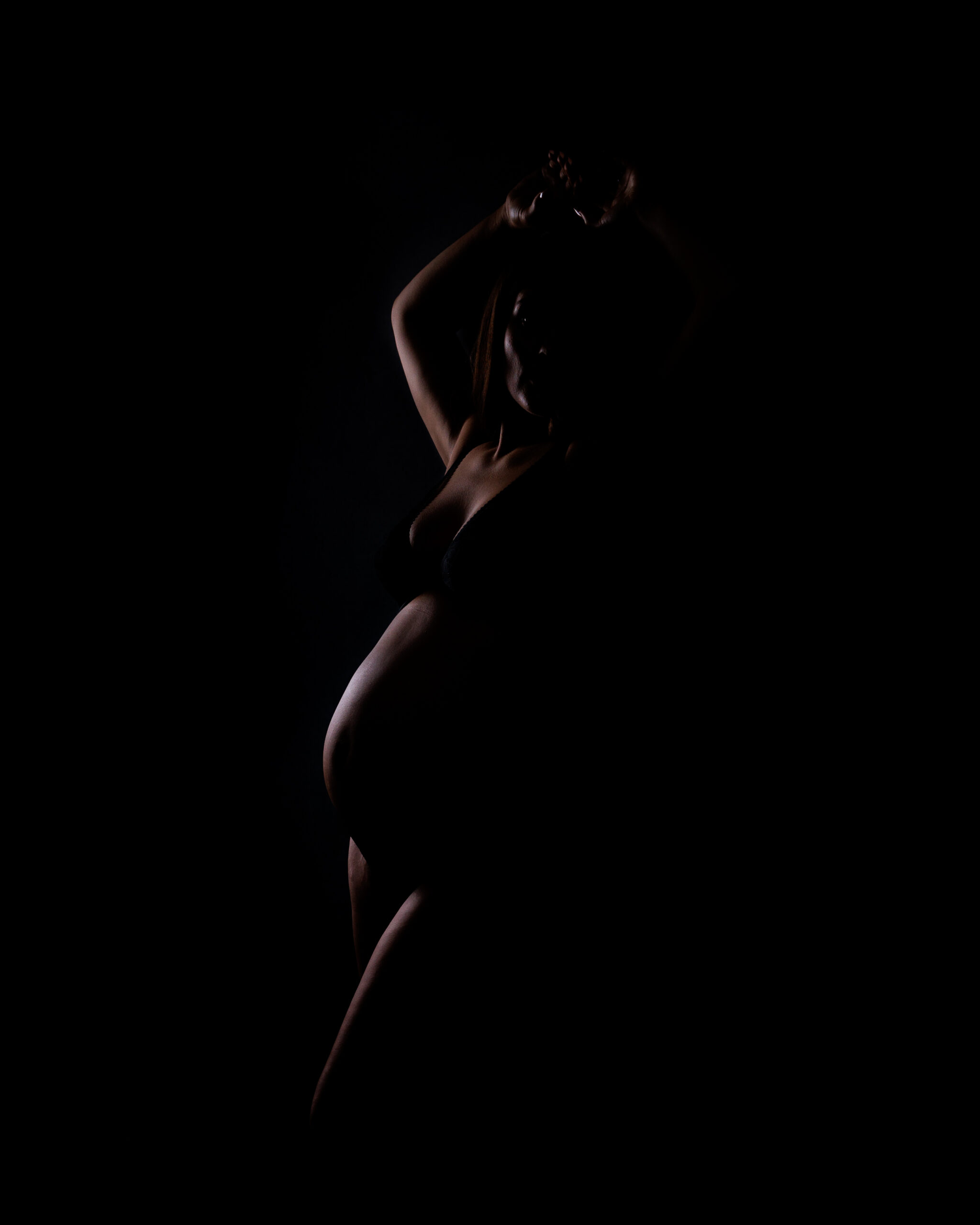 moody maternity portrait with dramatic lighting and intimate pose