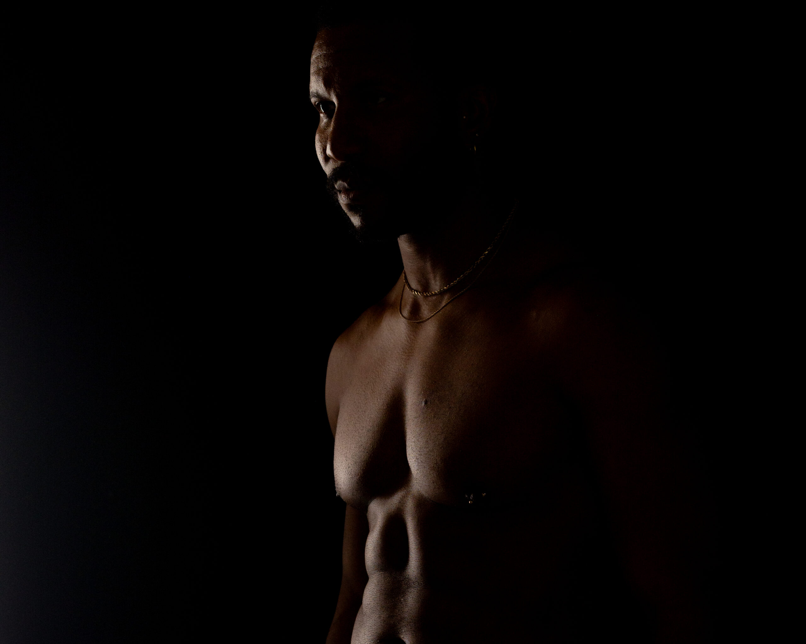 moody male boudoir portrait with dramatic lighting highlighting physique