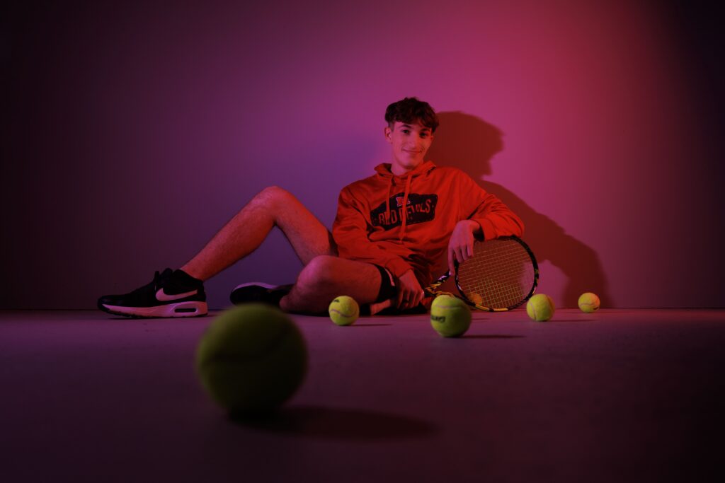 Indianapolis senior photographer captures tennis player portrait with colored studio lighting and racket