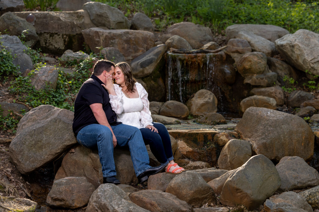 A couple sitting on rocks in front of a waterfall at Holcomb Gardens on Butler University, a top family photo location in Indianapolis