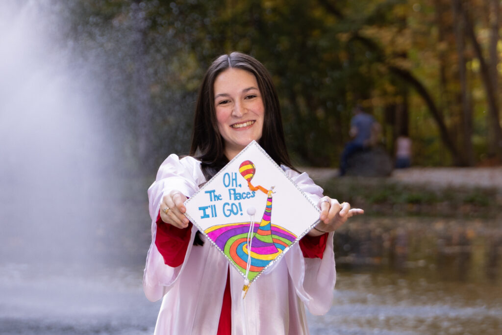 Senior girl holding a decorated graduation cap by a fountain, Indianapolis senior pictures by Dimensions Photography