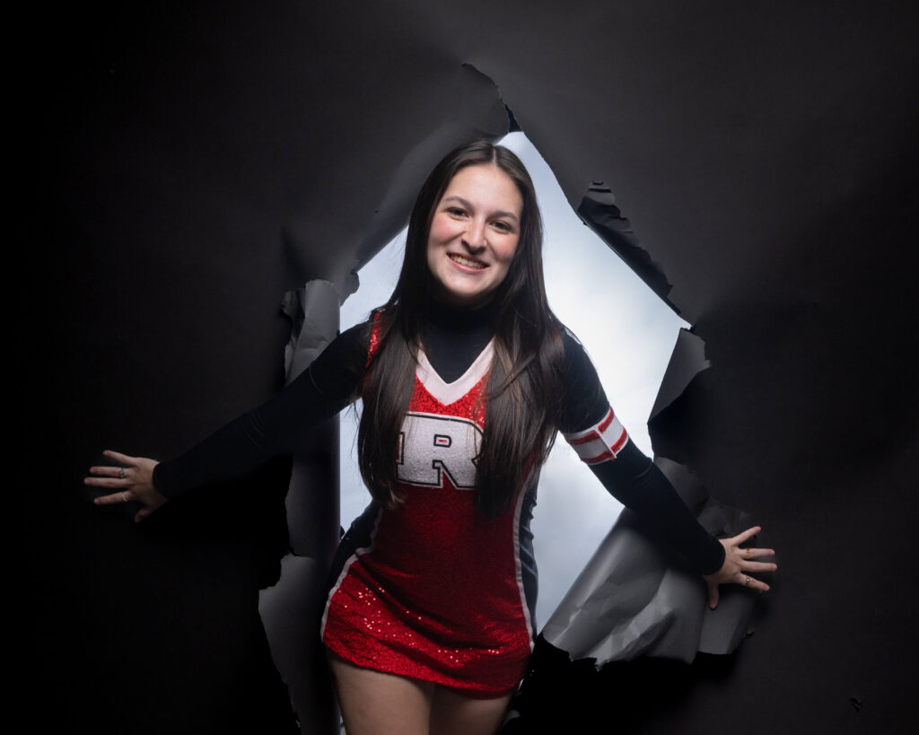 Senior cheerleader portrait bursting through a black paper backdrop, Indianapolis senior pictures by Dimensions Photography