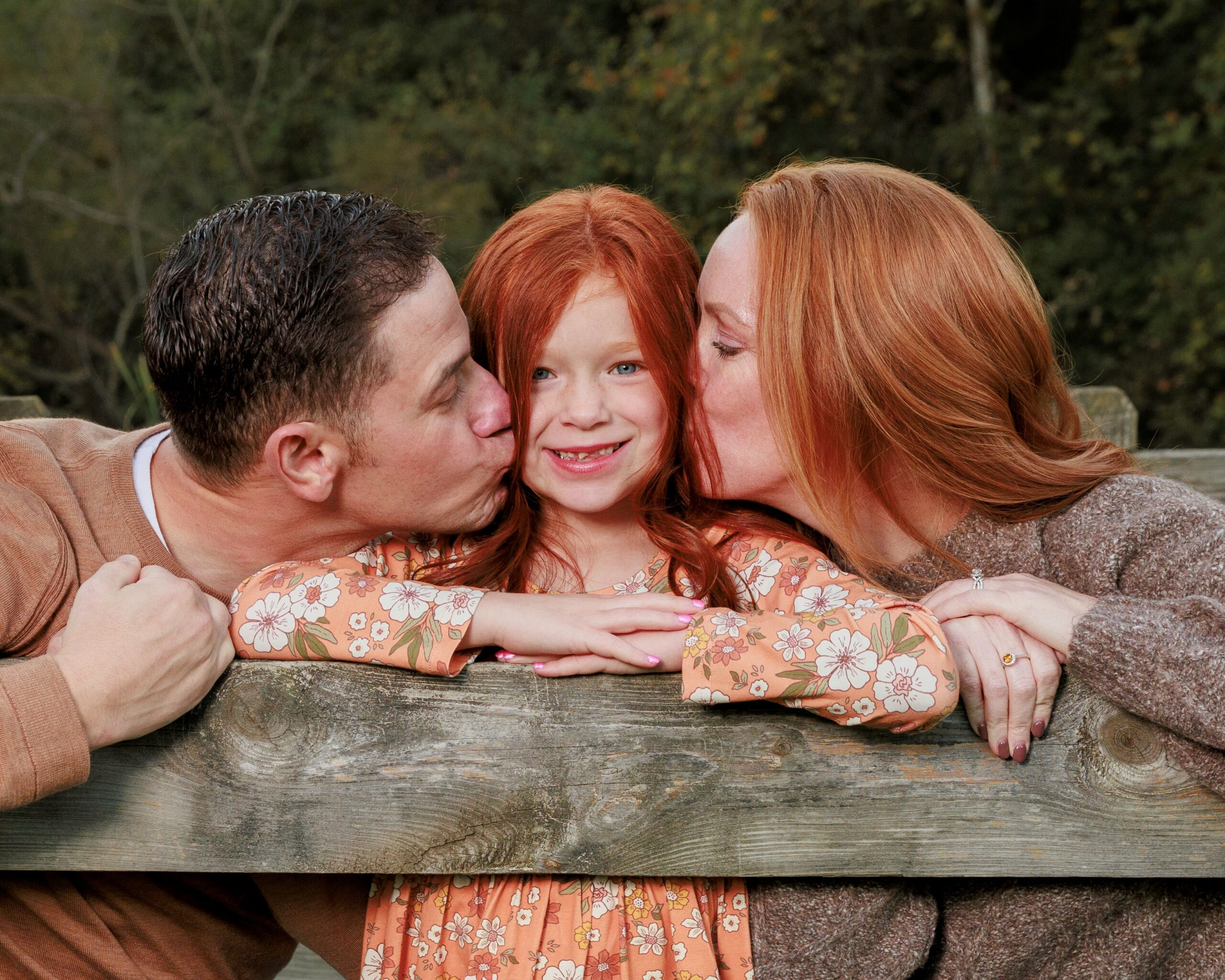 an indianapolis family photo of two parents kissing a little girl on the cheeks