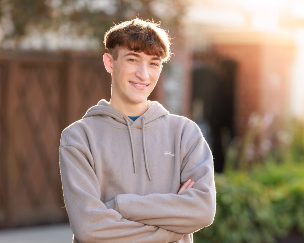 Indianapolis senior portrait of boy smiling outdoors during golden hour with arms crossed