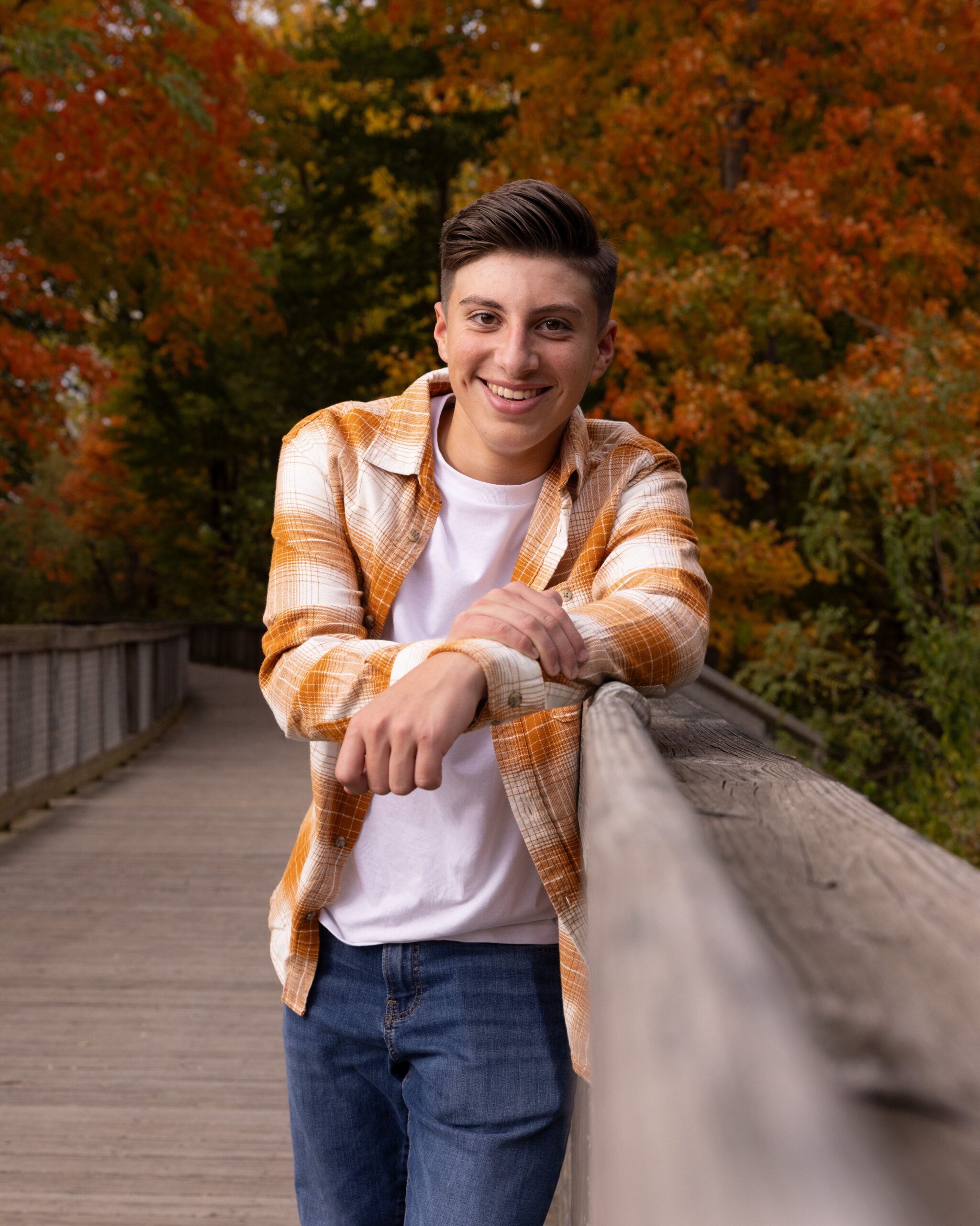 Teen boy leaning on a wooden boardwalk railing surrounded by fall foliage a fall family photo in indianapolis