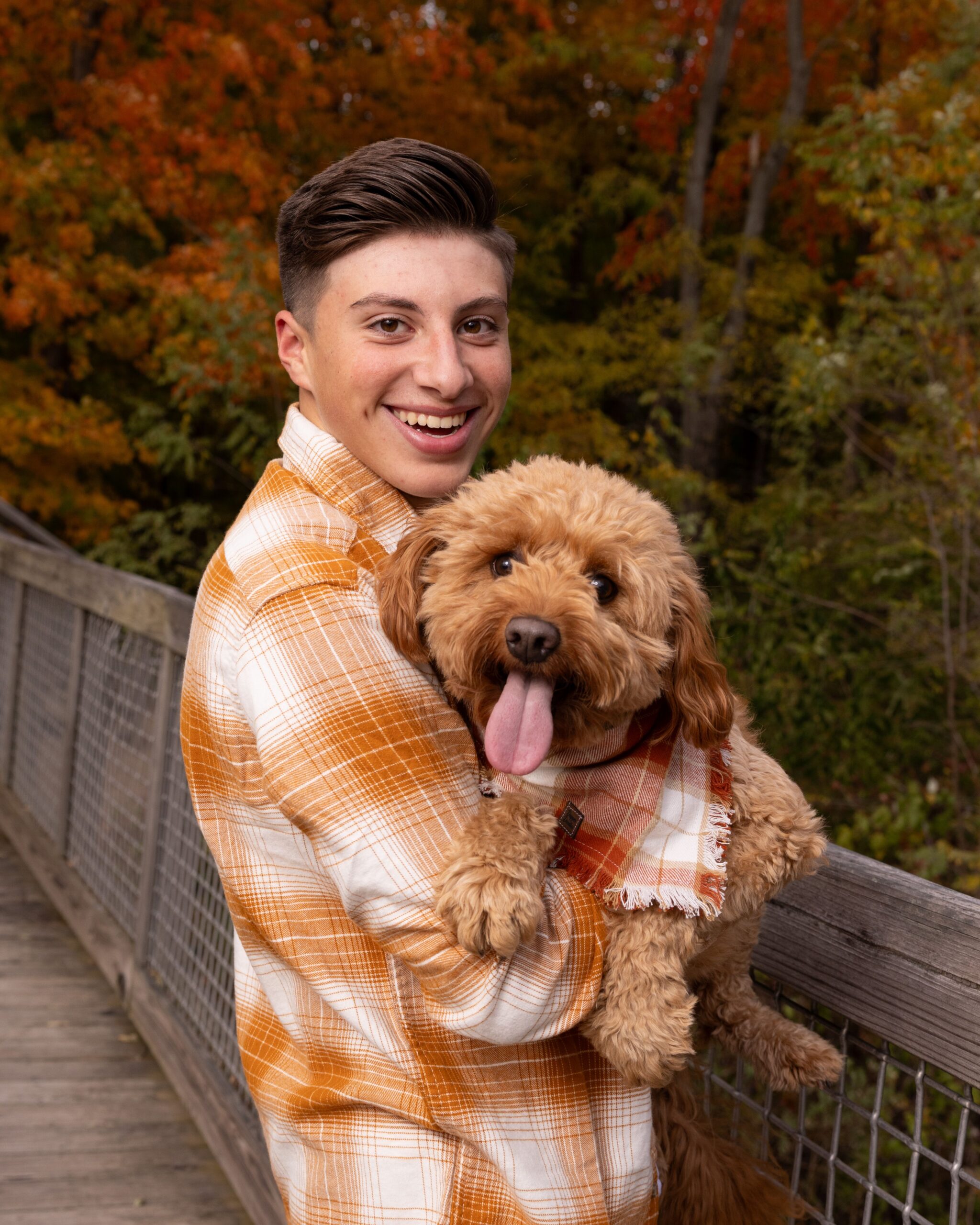 portrait of a teen boy holding his goldendoodle against colorful autumn trees