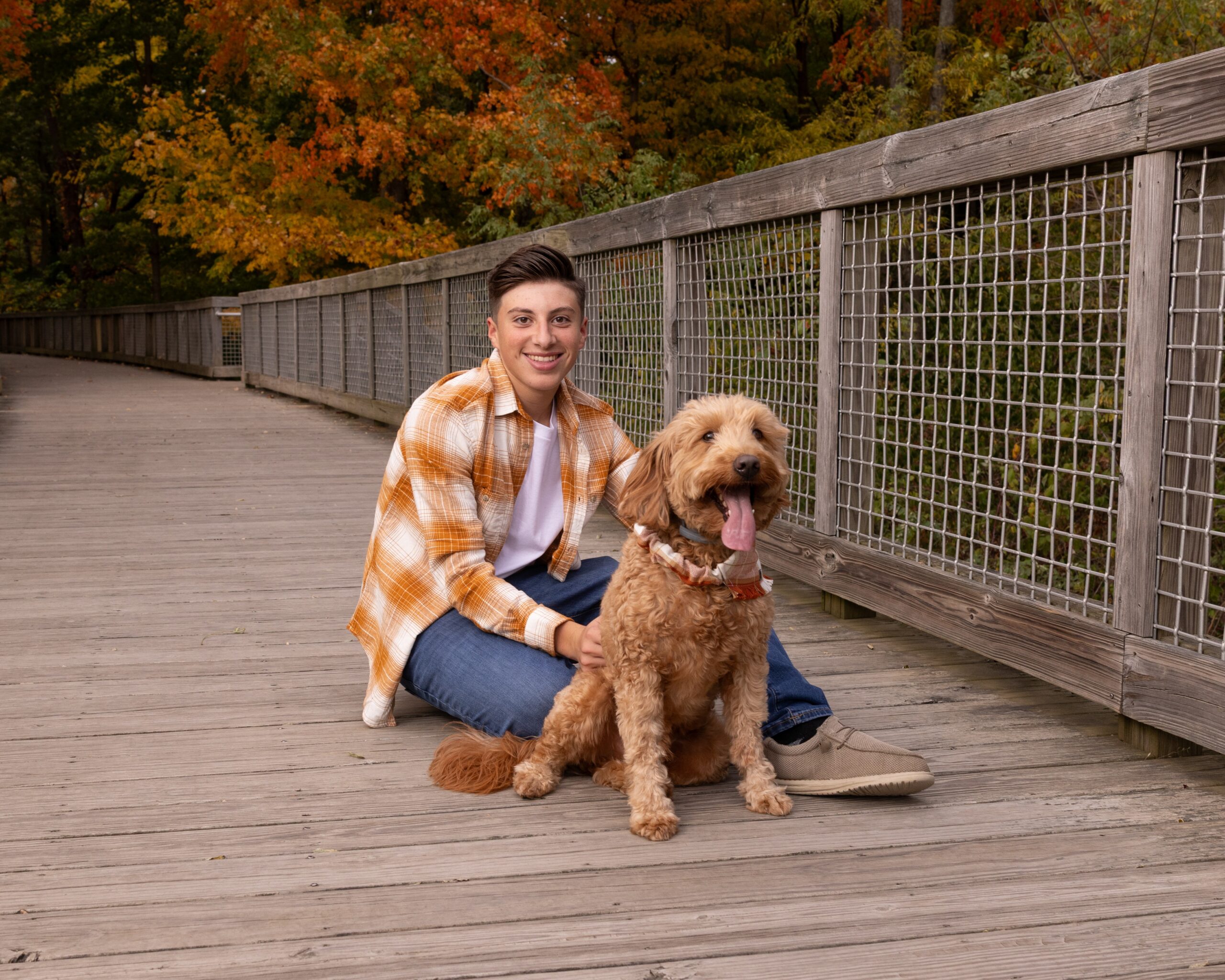 Teen boy sitting on a wooden boardwalk with his goldendoodle during a fall senior session