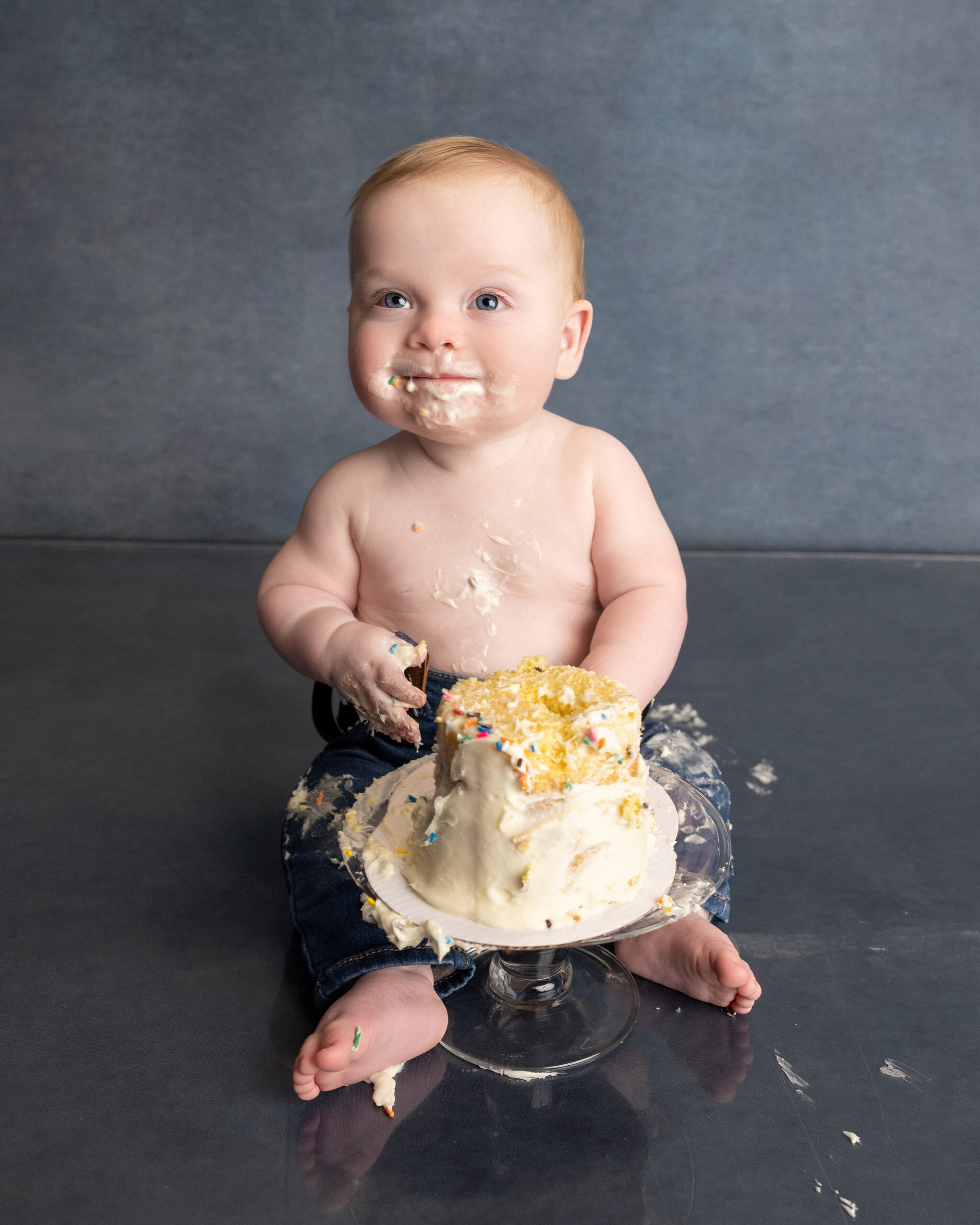 Baby smiling with birthday cake frosting on face and hands