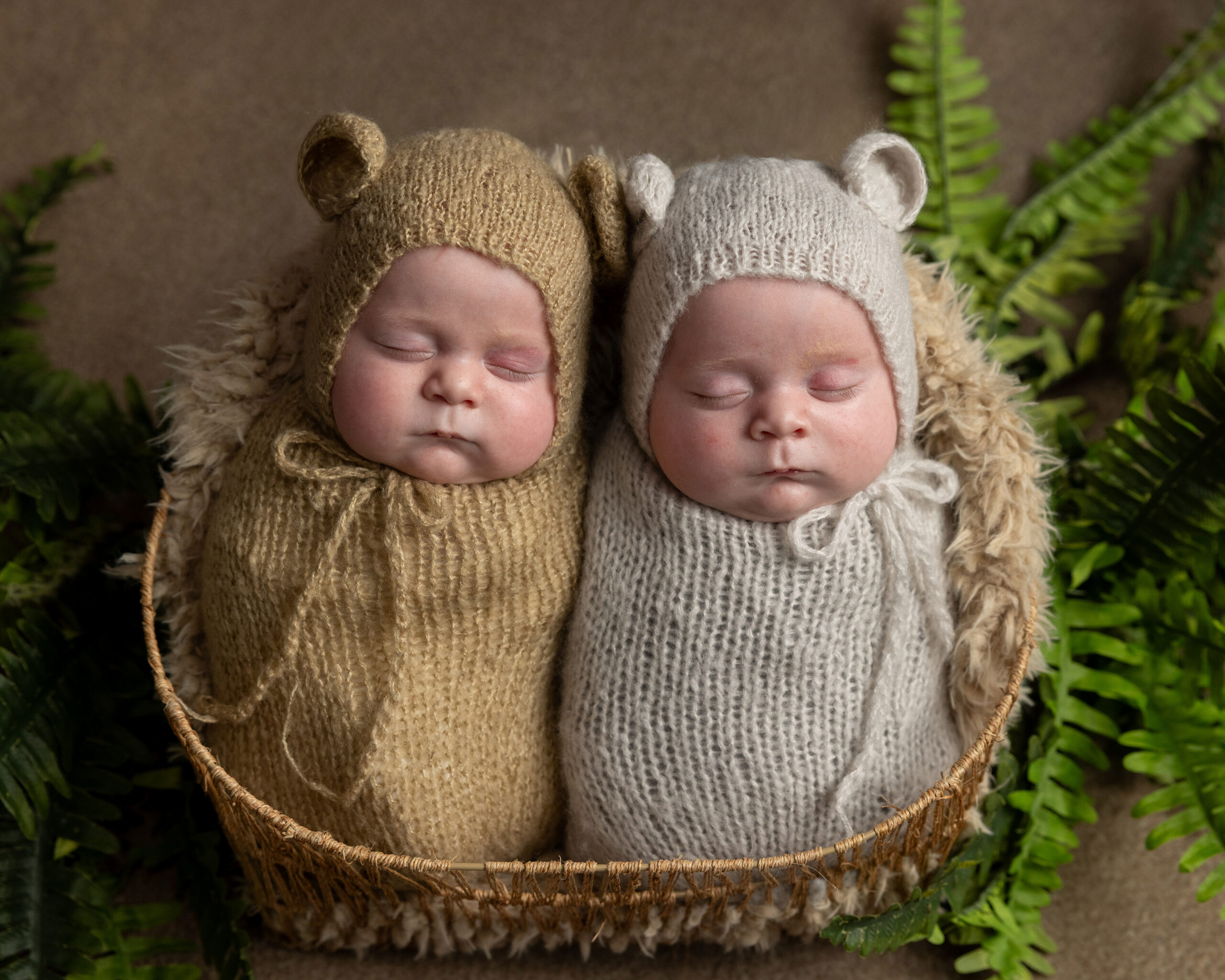 Twin newborns sleeping side by side in knit bear bonnets