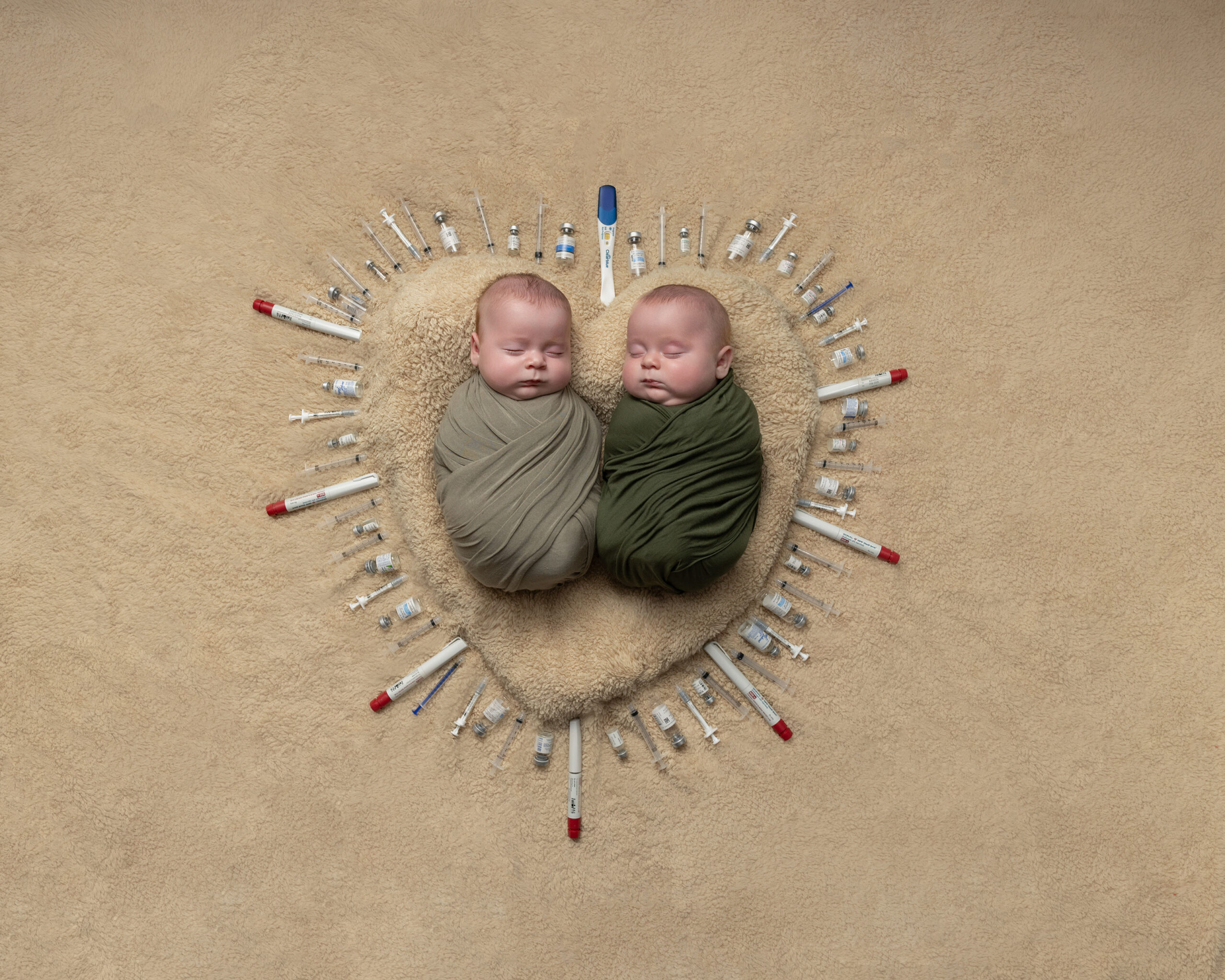 Twin newborns surrounded by fertility medication vials arranged in a heart shape