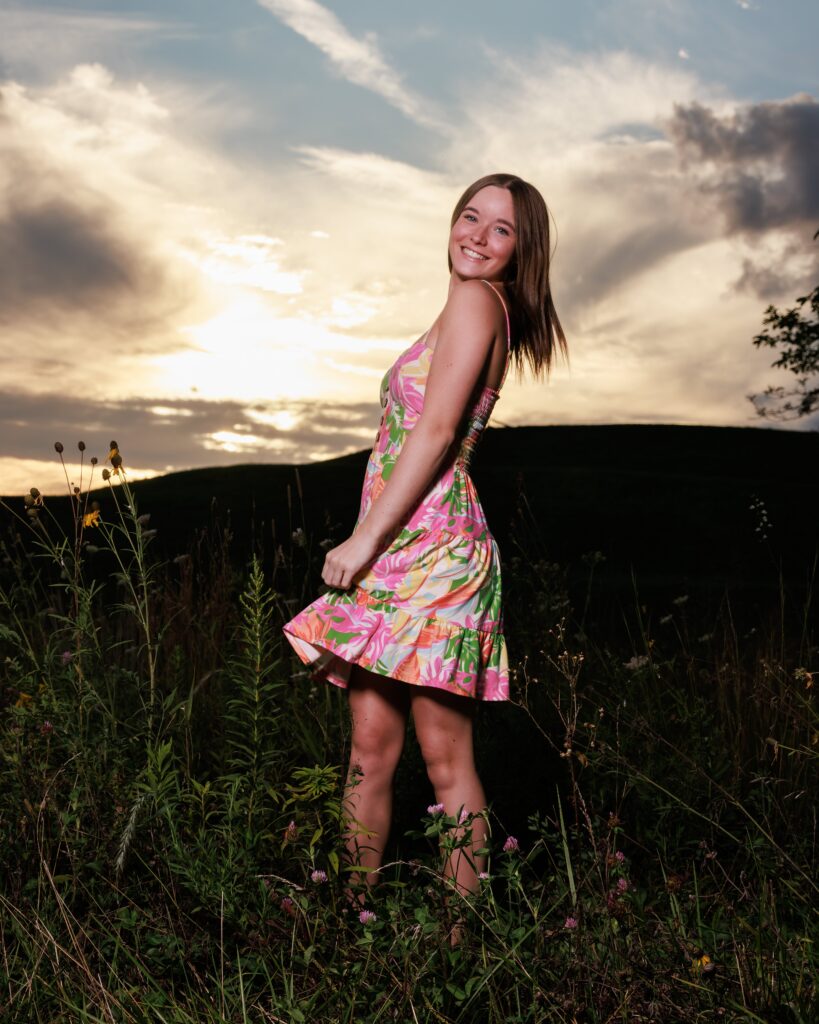 portrait of a girl in a floral dress twirling in a field at sunset