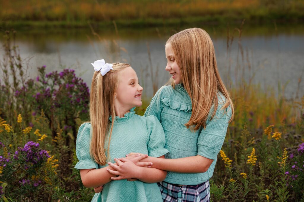 Two sisters in matching mint sweaters laughing together in a golden autumn field