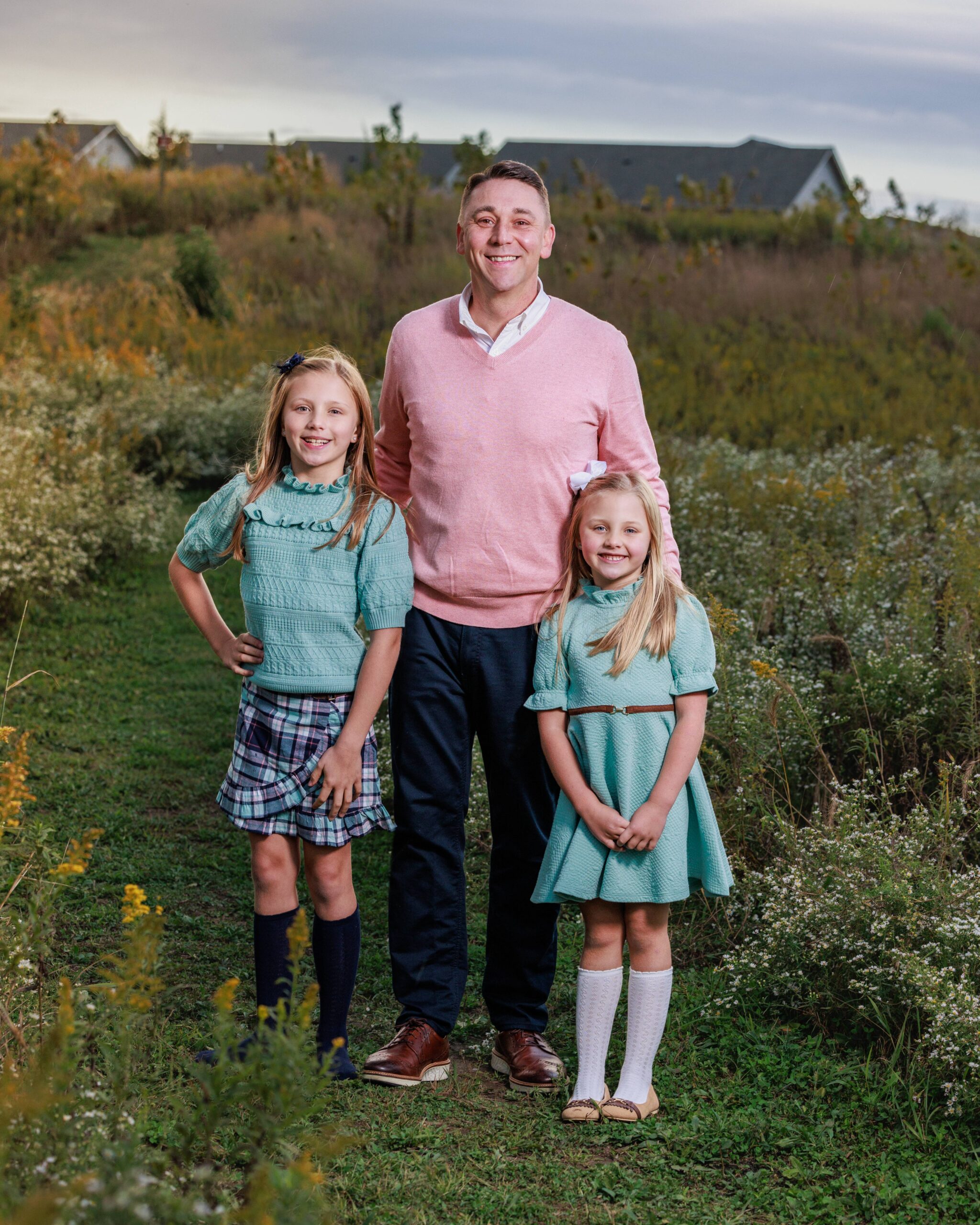 Father smiling with his two daughters in a golden field at sunset during a fall family photos session