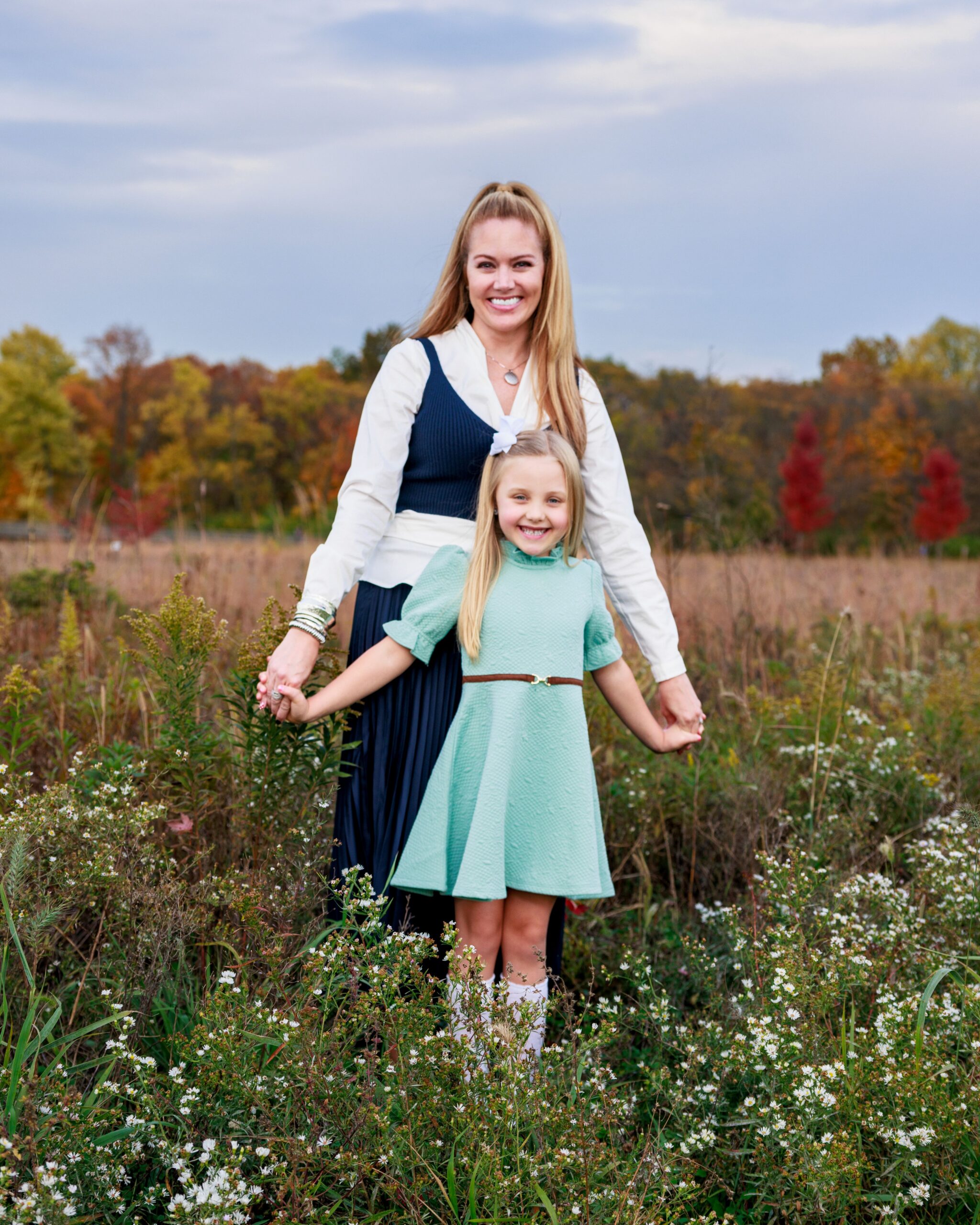Mother and daughter holding hands walking through a wildflower field in fall