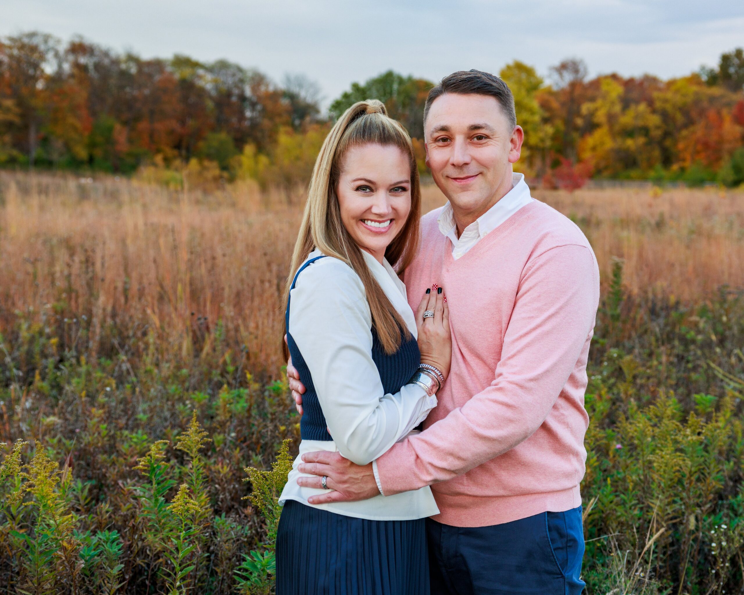 Husband and wife embracing in a golden autumn field during a family photography session