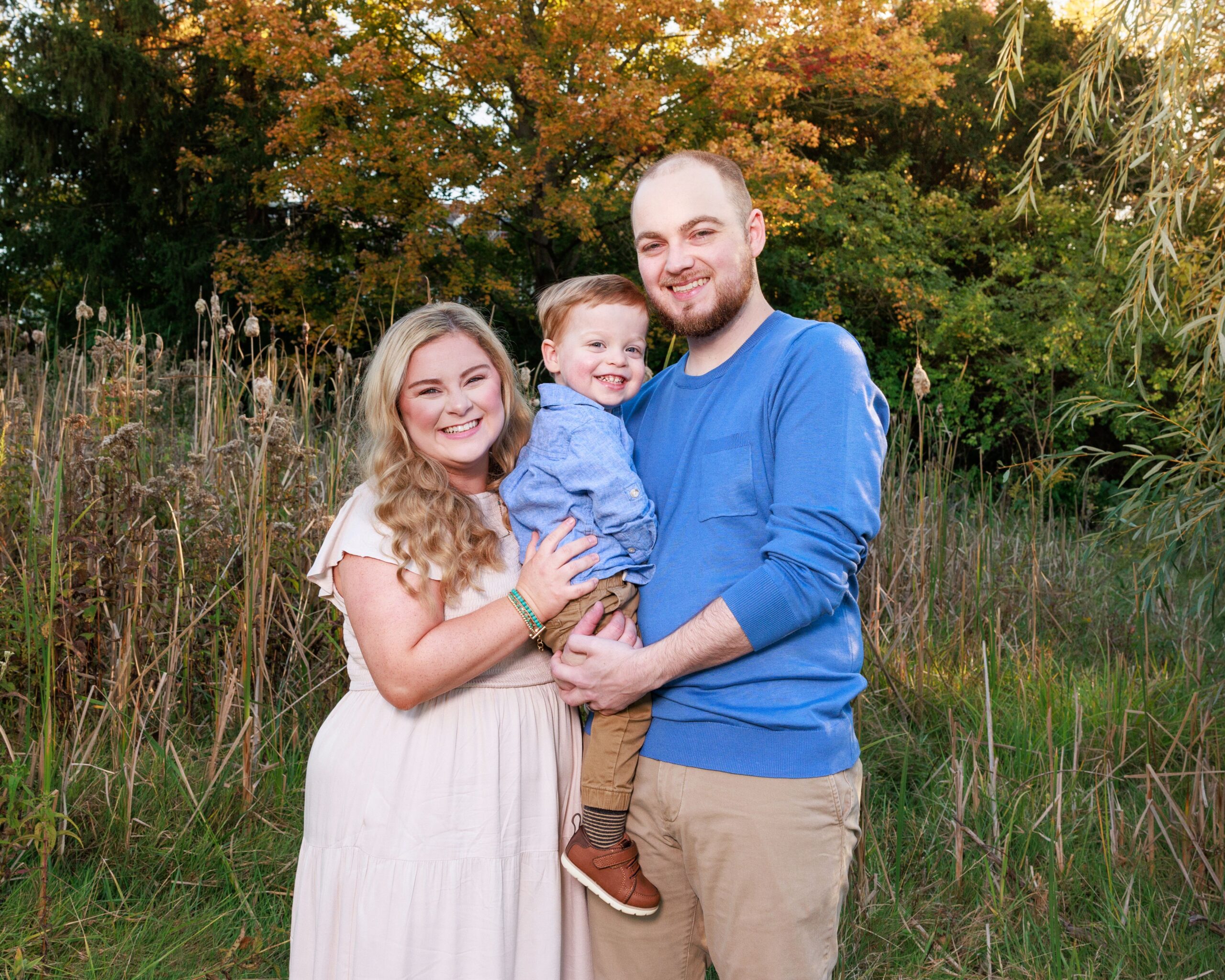 Family of three smiling together near tall marsh grass during a fall family photography session