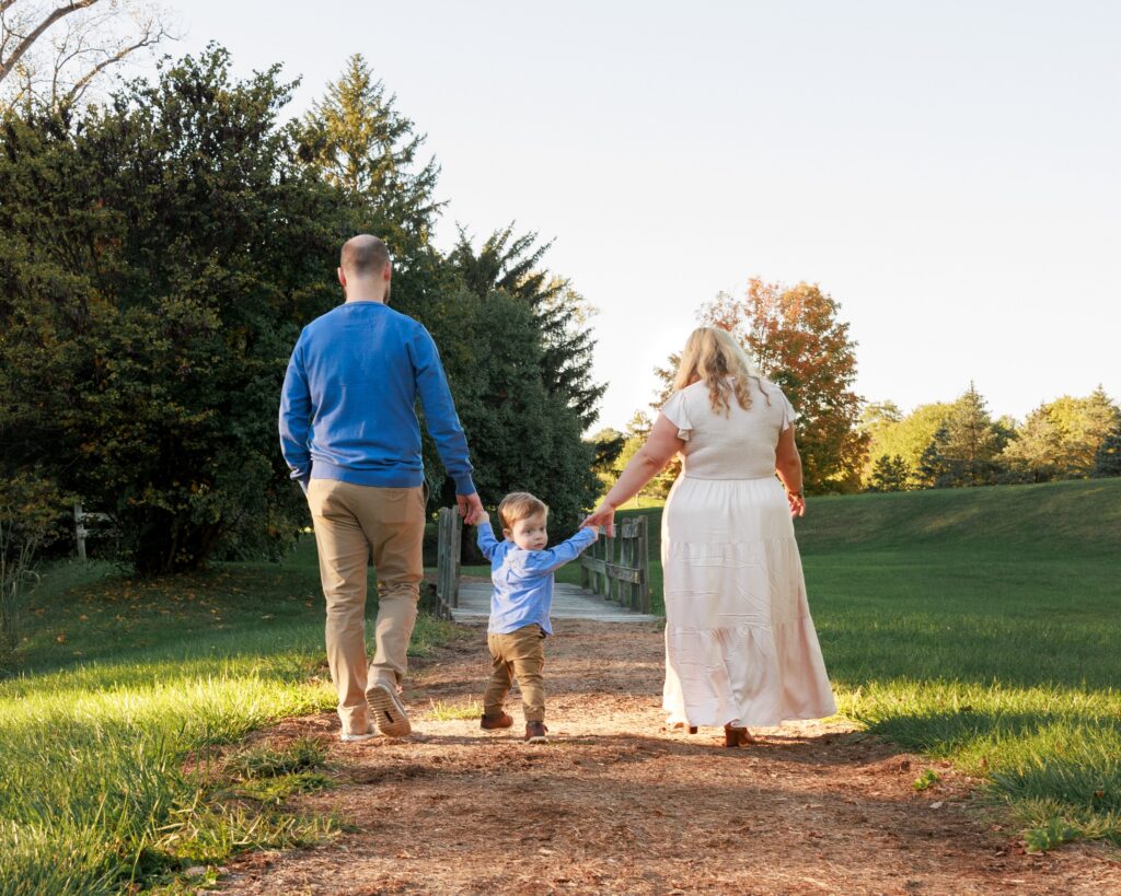 Family of three walking hand in hand down a path during golden hour