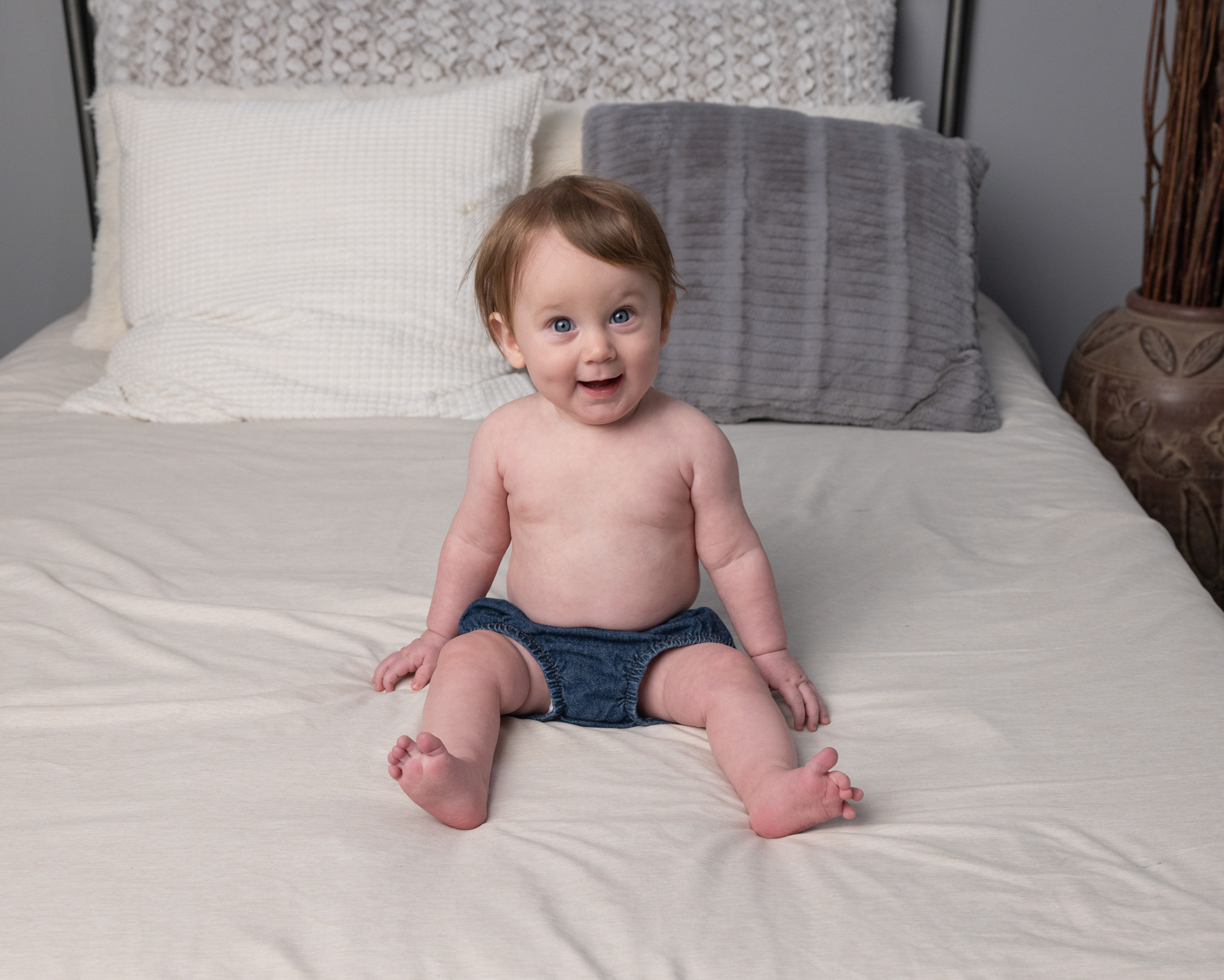 Baby boy in denim shorts smiling on a bed during his sitter session photography appointment