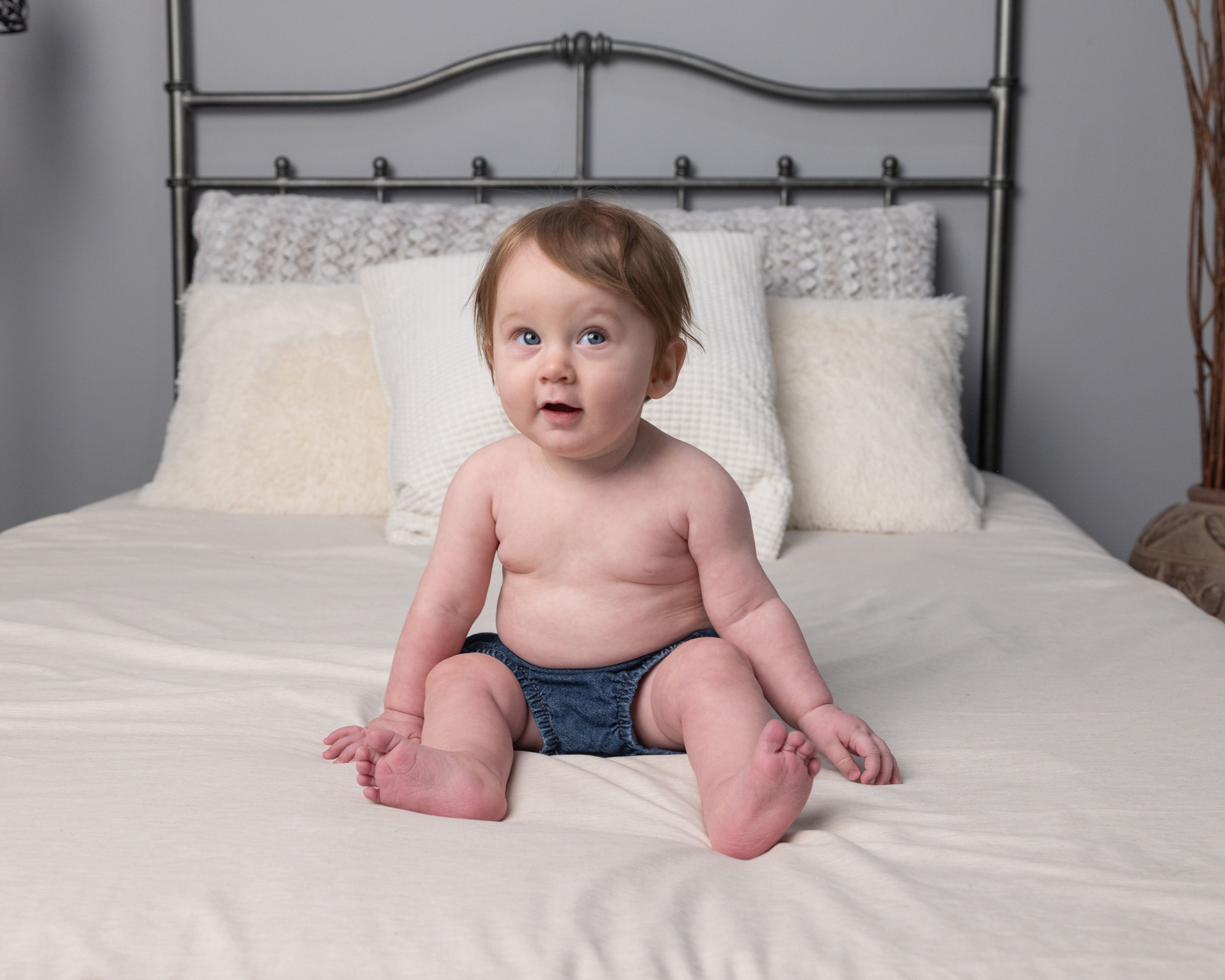 Baby boy sitting on a bed with an open-mouthed, curious look