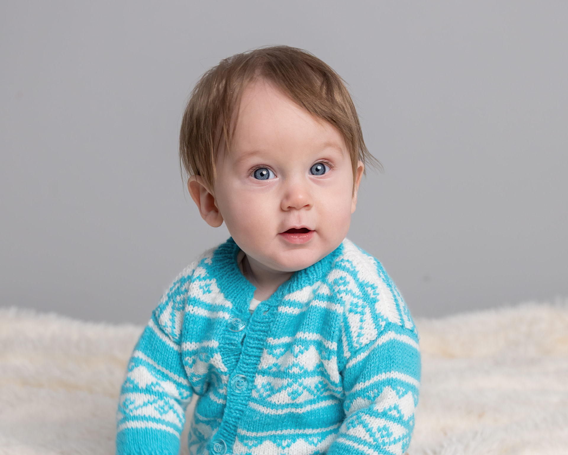 Close-up of baby boy in teal cardigan against a soft gray studio backdrop