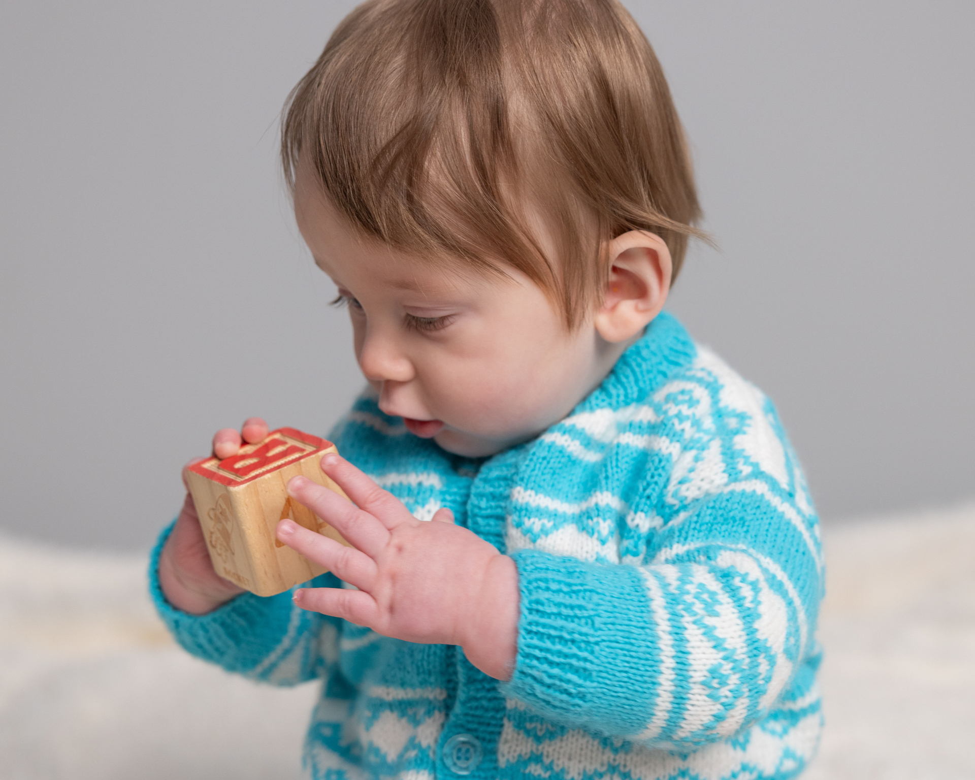 Baby boy's hands gripping a wooden alphabet block during a sitter session