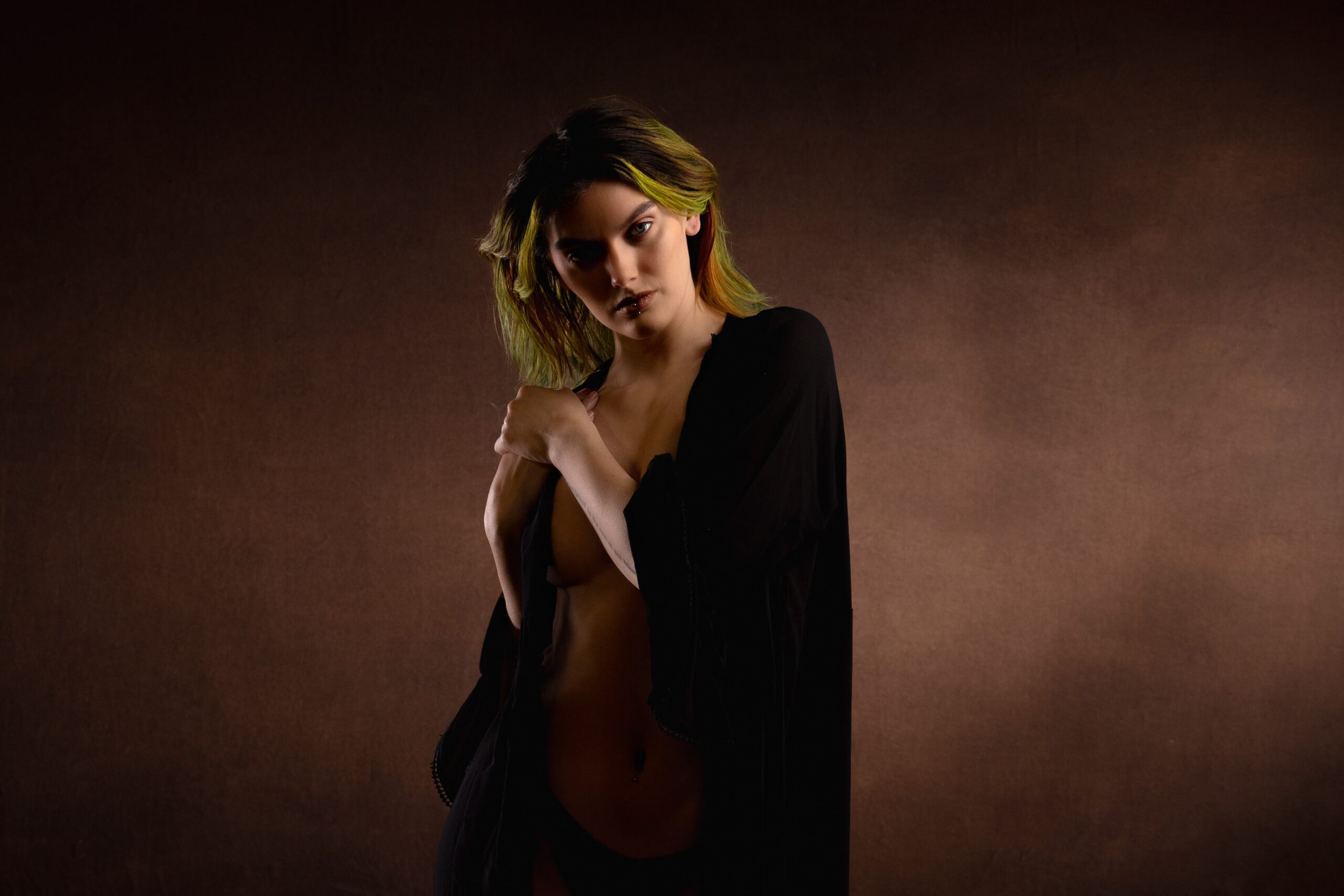 Soft warm light glows against a rich brown studio backdrop in a quiet boudoir frame
