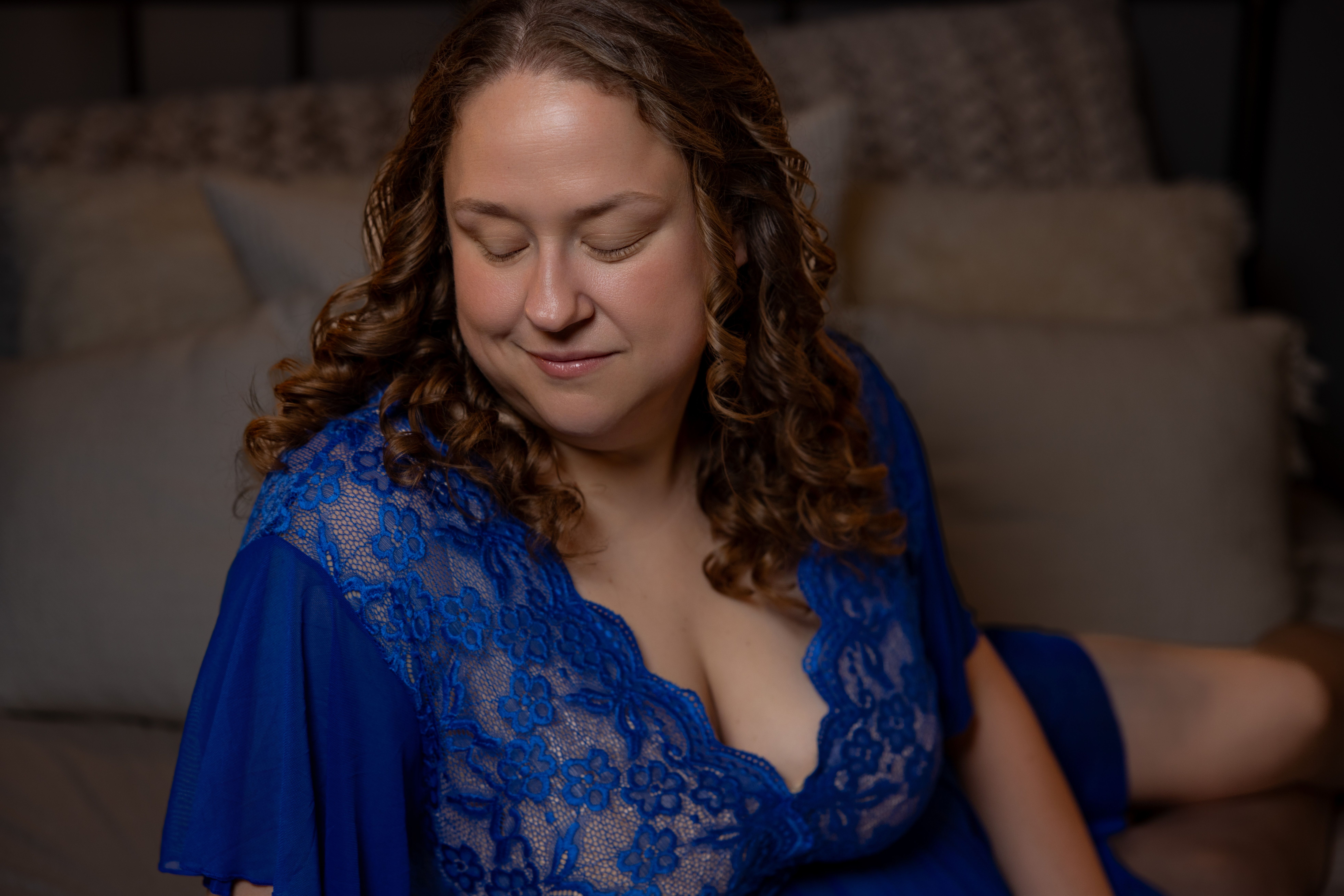 Soft lamplight and deep blue tones fill a quiet bedroom corner during a boudoir session